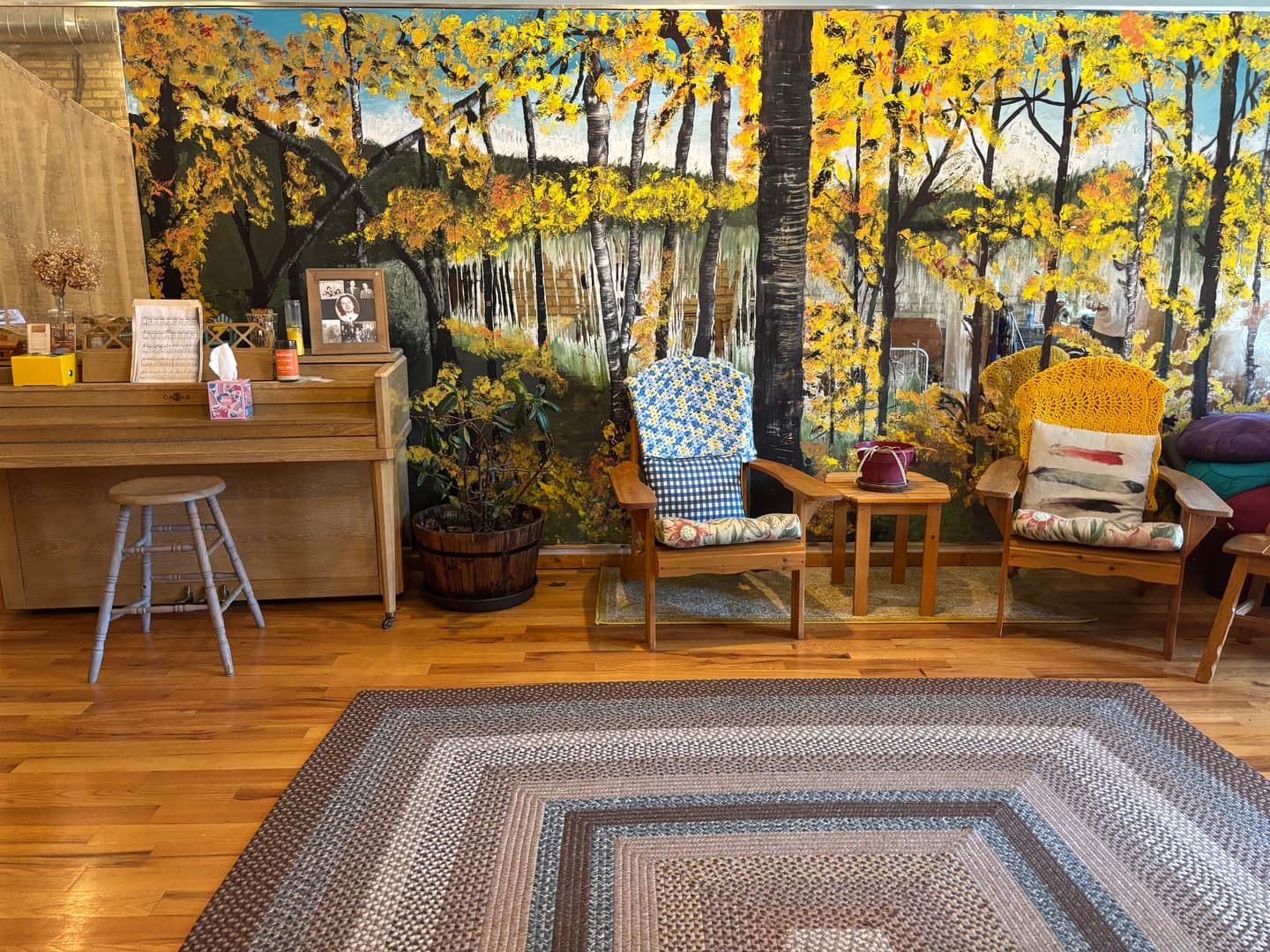 A reading corner framed by an autumn-woodland mural and comfortable chairs